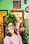 En leende kvinna med glasögon håller upp en grön växt i en färgstark lokal.