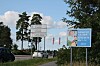 Vägskyltar och en blå reklamskylt står vid en grönskande väg i Lojo.