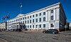 Helsingfors stadshus med flaggor, gatsten och en bil framför byggnaden.