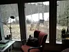Röd fåtölj i ett ljust uterum med snötäckt skog synlig genom fönstren.