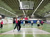 Skolelever spelar basketboll i en stor idrottssal med korg och gröna planer.