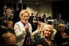Kvinna håller mikrofon och talar till publik i ett inomhusrum.