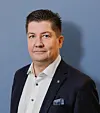 Man i mörk kostym och vit skjorta framför blå bakgrund.