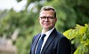 Pääministeri Petteri Orpo seisoo ulkona puiden ja lehtien keskellä tummassa puvussa.