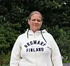 Företagaren Ragna-Lise Karlsson står framför grönskande träd i en vit Bromarv Finland-hoodie.