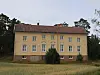 Gul gammal skolbyggnad med rött tak som står övergiven vid en gräsplan.