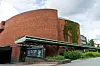 Rött tegelklätt Kulturhuset med låg glasentré och grönväxt på fasaden under en molnig himmel.