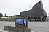 Seinäjoki stadshus i mörkt tegel vid ett stenlagt torg, med en informationsskylt i förgrunden.
