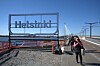 Helsinki-skylt vid en bro med en fotgängare på trottoaren.