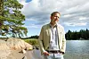 Man vid Vitsands klippiga strand utanför Ekenäs, med skog och lugnt vatten i bakgrunden.