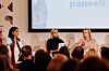 Tre kvinnor deltar i en paneldebatt inför publik med en presentationsskärm bakom sig.
