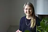 Psykologen Marjo Lehtinen ler framför kameran i ett ljust rum med en grön växt.