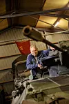 Sten Johansson står vid ett grönt pansarfordon i en museihall med en röd sovjetisk flagga i bakgrunden.