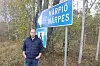 Man bredvid blå vägskylt mot Närpiö och Närpes i en lövskog.