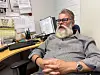 Kennet Lundström sitter i en kontorsstol vid ett skrivbord med papper och anslag bakom sig.